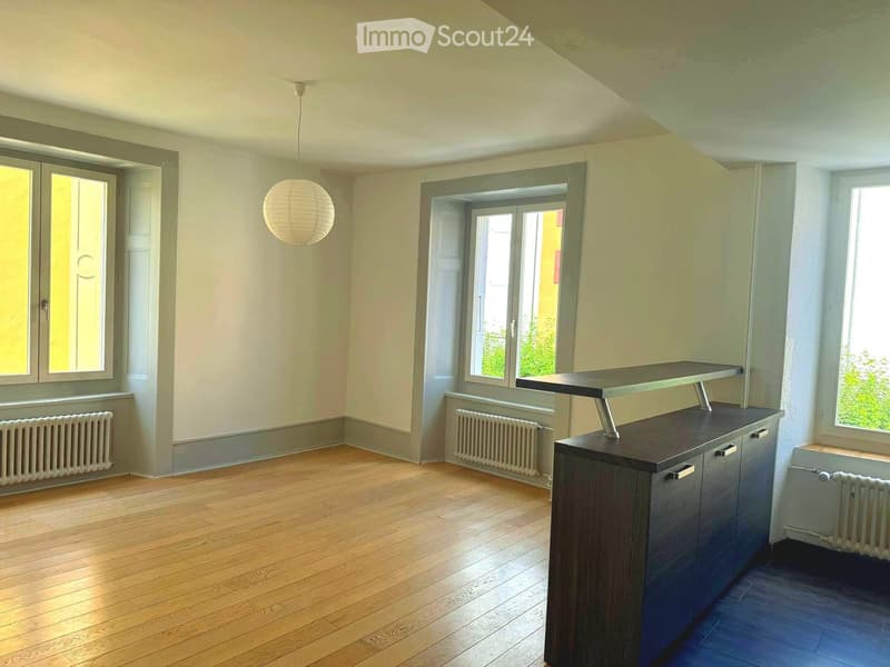 Bright, unfurnished room with wooden flooring, large windows, and a modern kitchen island with cabinets.