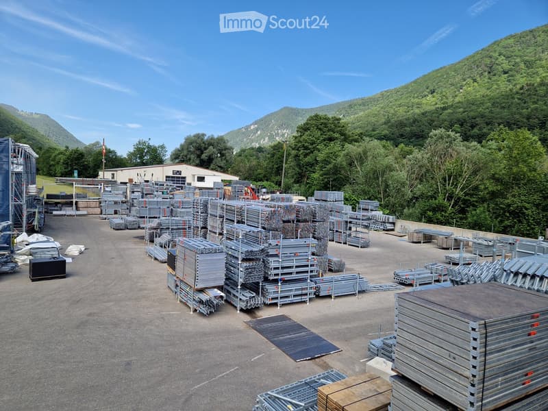 Outdoor construction site with stacks of metal scaffolding, beams, and materials, surrounded by trees and mountains.