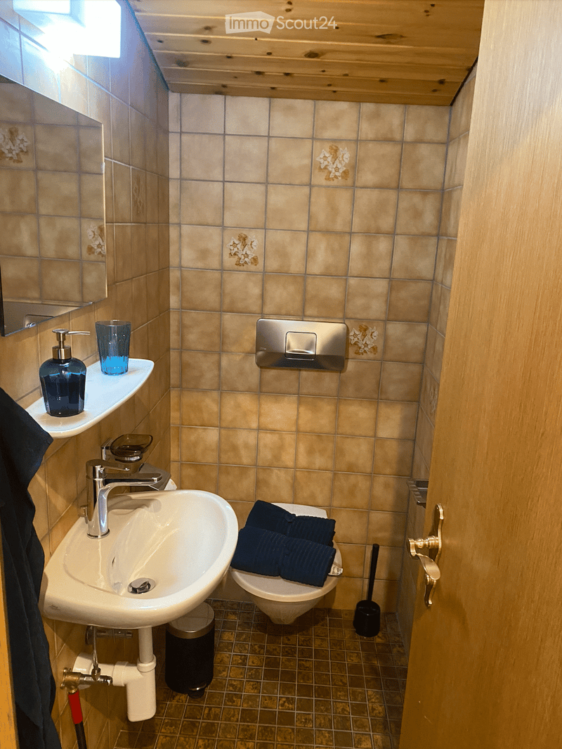 A small bathroom, white tiled walls, a white sink, toilet, mirror, and towel rack.
