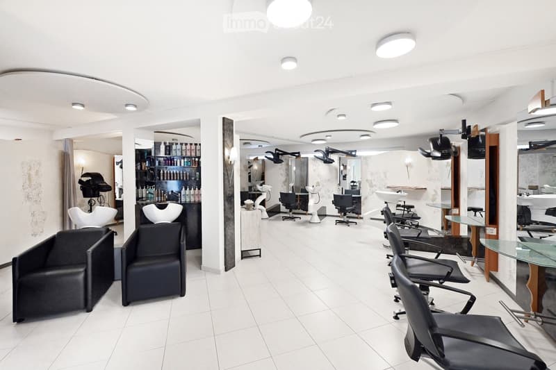 Modern salon with white tiled floors, multiple black and white chairs, mirrors, shelves with hair products, and a reception area with a glass table.