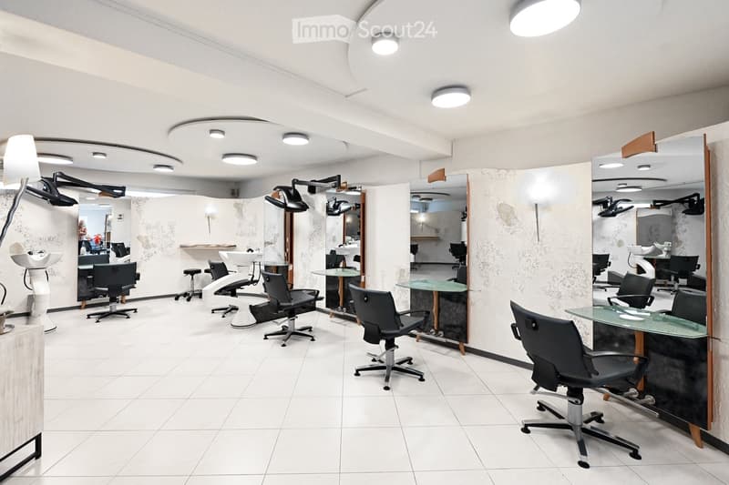 Modern salon with white tiled floors, multiple black salon chairs, mirrors, sinks, and a reception desk.