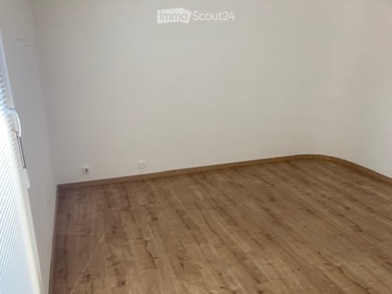 Empty room with wooden flooring and white walls, featuring a radiator and window with blinds.
