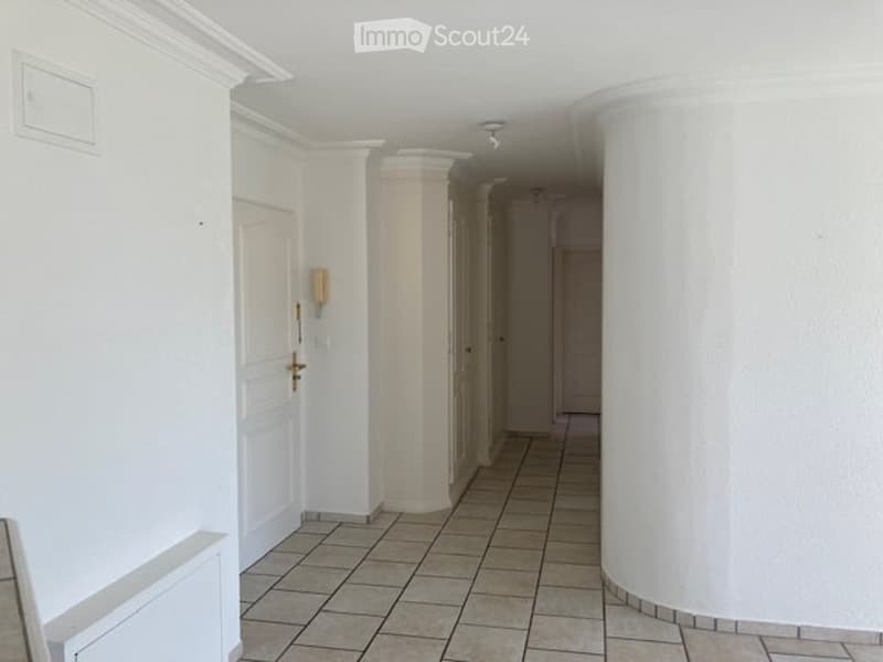 Empty hallway with white walls, tiled floor, and several doors. Minimalist design with a single light fixture on the wall.