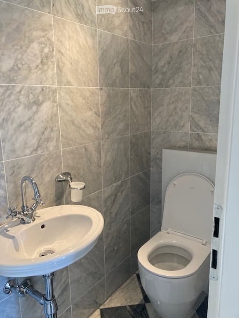 Modern bathroom with marble tiles, white sink, chrome faucet, and toilet with open lid.