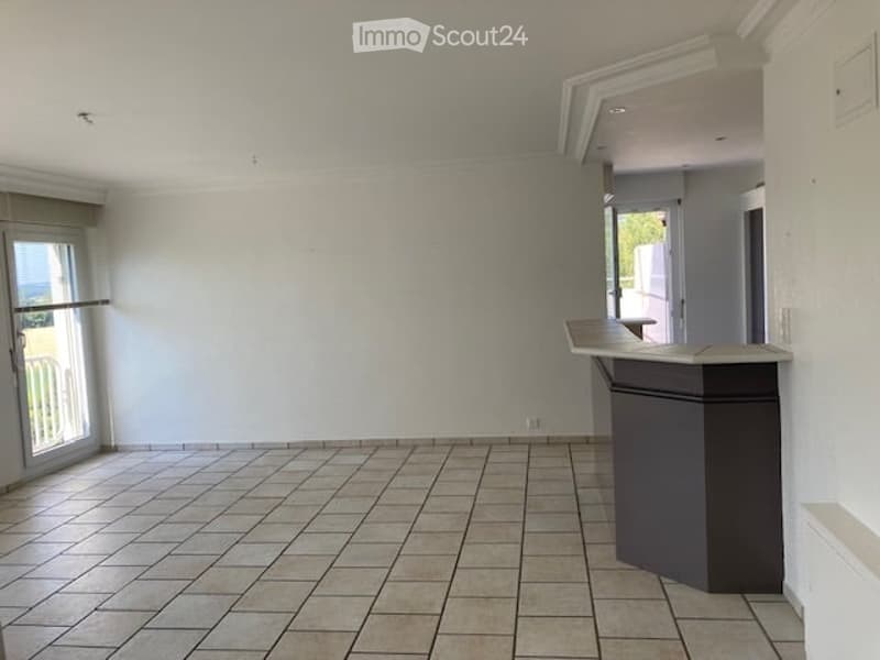 Empty room with tiled floor, white walls, and a single reception desk near a glass door leading to a balcony.