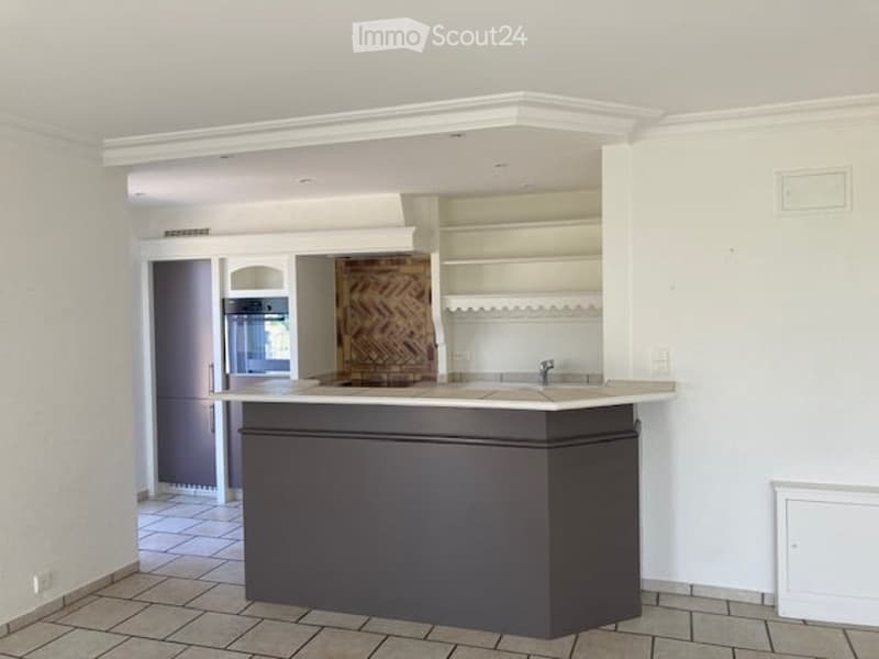 Empty kitchen area with a central island, white walls, and tiled flooring. No furniture or appliances are present.