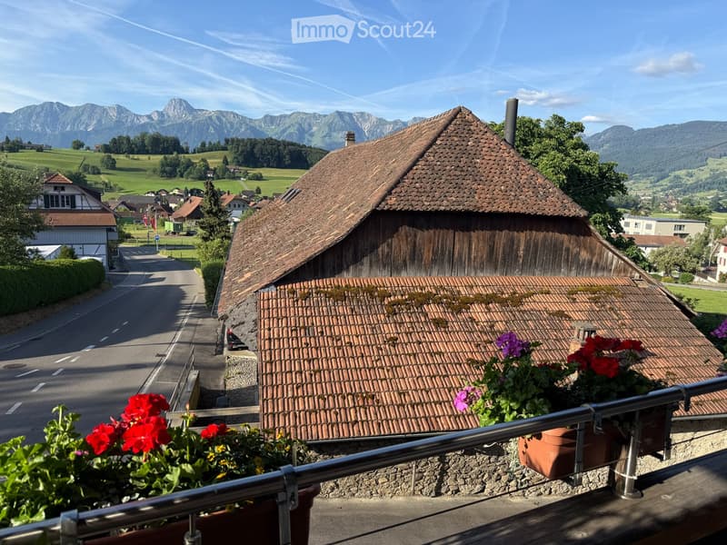 Balcony overlooking a picturesque village with traditional wooden houses, tiled roofs, and distant mountains.