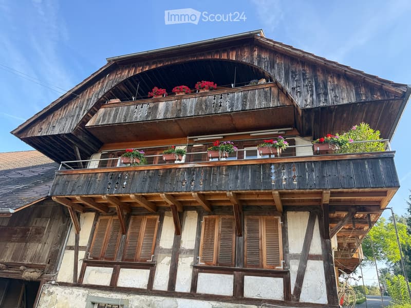 Traditional wooden house with multiple balconies adorned with potted flowers, featuring wooden shutters and a classic architectural style.