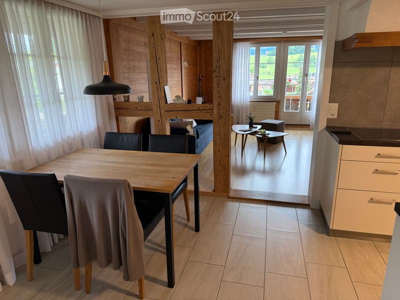 Open-plan living and dining area with wooden floors, large windows, and modern furniture including a dining table, chairs, sofa, coffee table, and pendant light.
