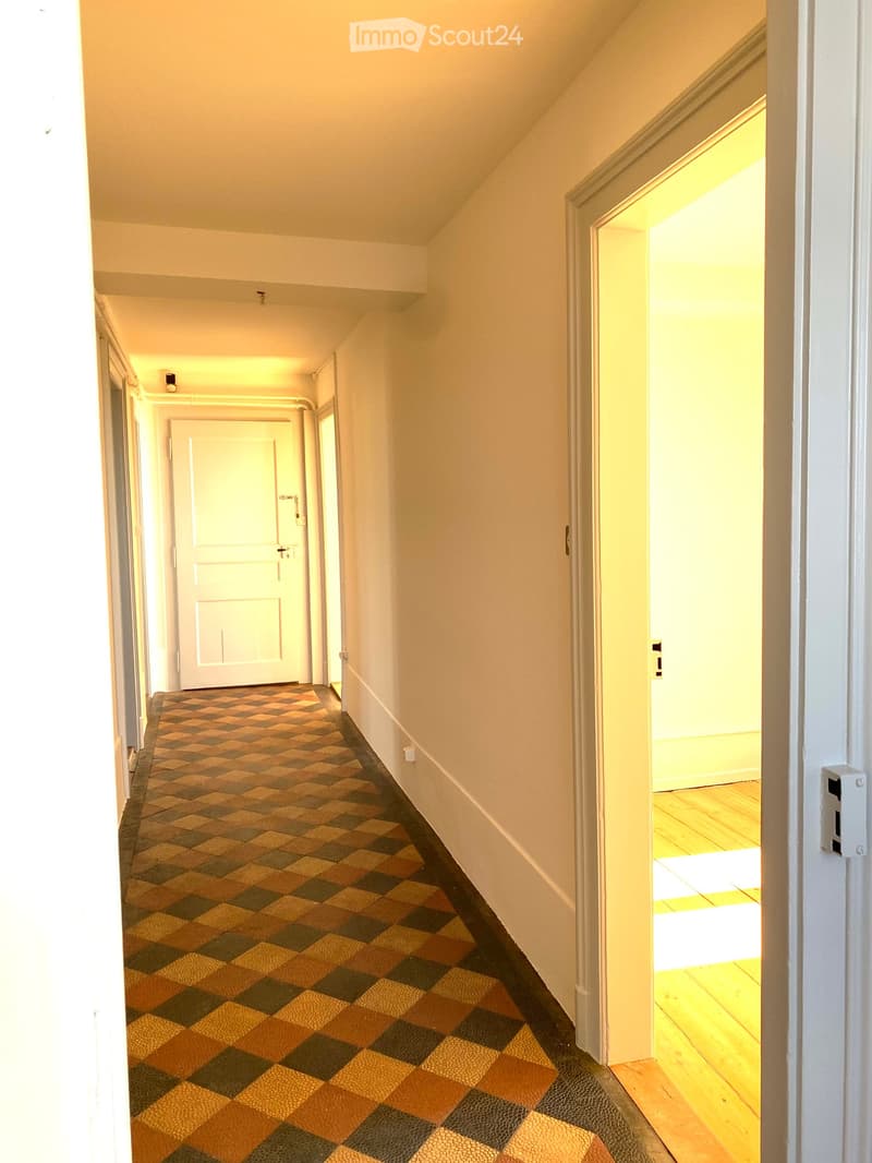 A narrow hallway with a checkered carpet, white walls, and several doors leading to other rooms.