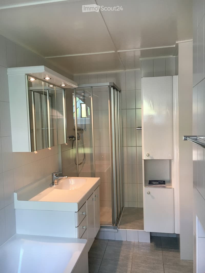 Modern bathroom with white tiles, a large mirror, a sink with a modern faucet, a bathtub, and a glass-enclosed shower area.