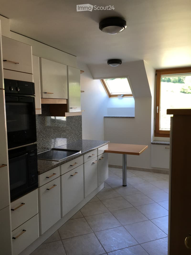 Modern kitchen with white cabinets, granite countertops, induction stove, built-in oven, and a small wooden table.