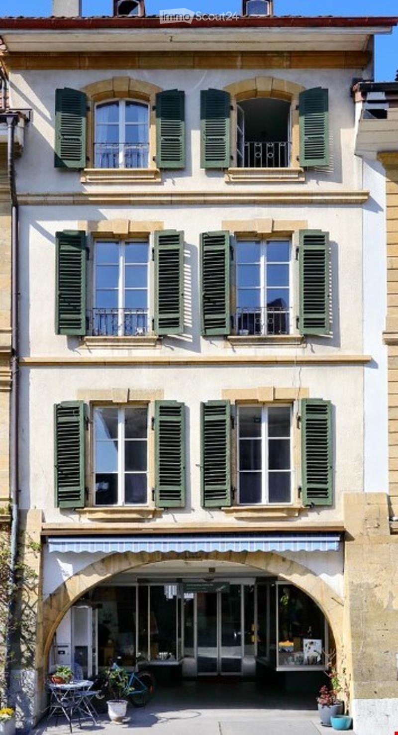 Classic European-style building with green shutters, arched entrance, and small outdoor seating area.