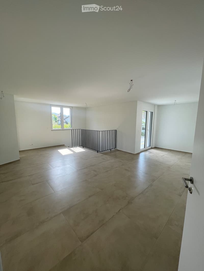 Empty room with tiled floor, white walls, and large windows, featuring a metal safety barrier near the window.