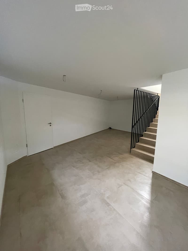 Empty room with white walls, tiled floor, and a staircase leading upwards with a black railing.