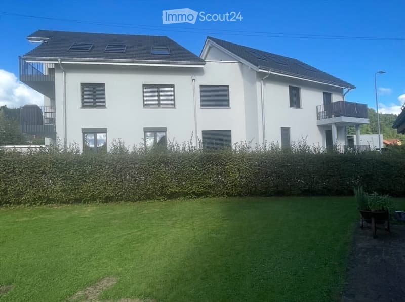 Modern two-story white house with multiple windows, balconies, and a well-maintained lawn in front.