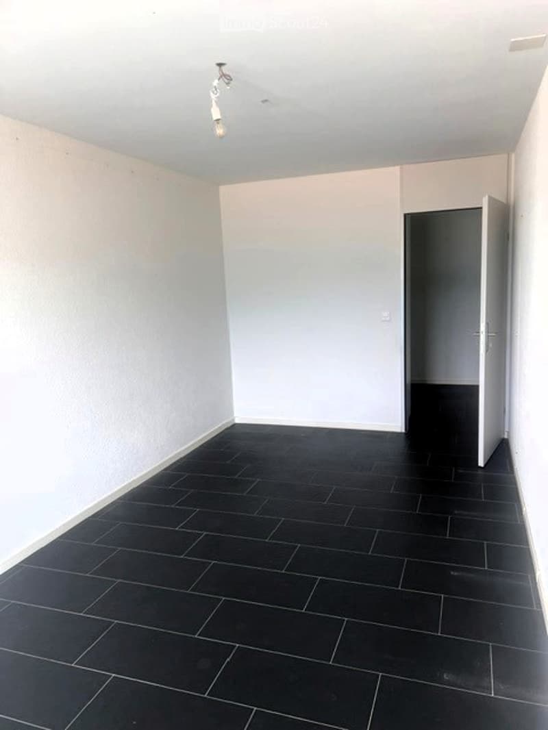 Completely empty room with white walls, black tiled floor, and a single light fixture on the ceiling. No furniture or equipment.