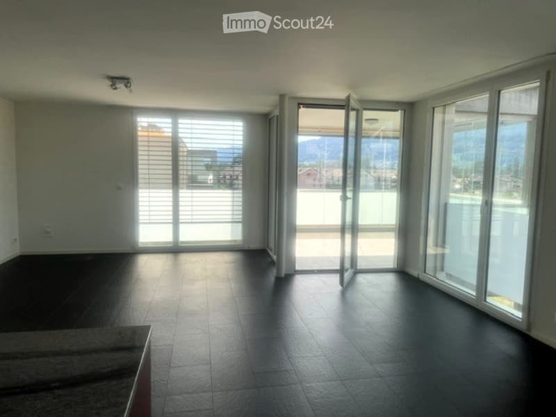 Empty room with large windows and sliding glass doors leading to a balcony, featuring a dark tiled floor and white walls.