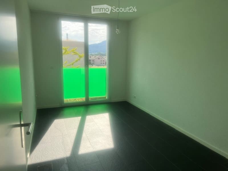 Empty room with dark flooring and large sliding glass door leading to a balcony with a view of mountains and greenery.