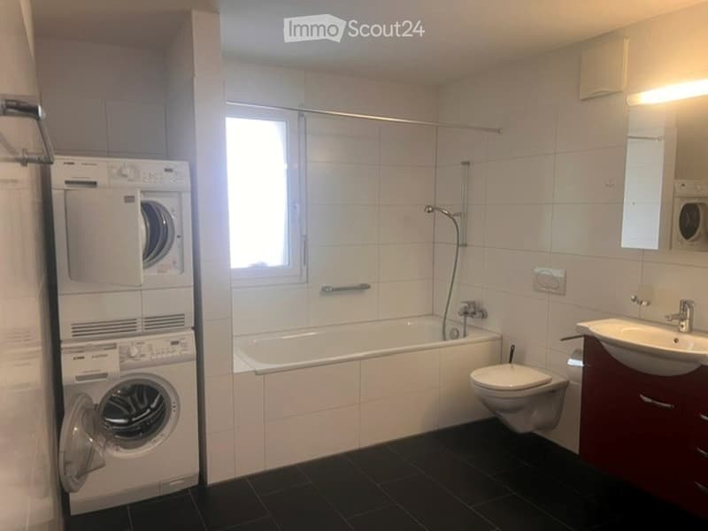 Modern bathroom with white tiles, a bathtub, toilet, sink, mirror, and a private washing machine.