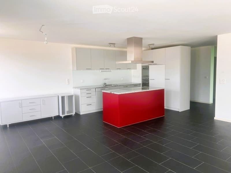 Modern kitchen with white cabinets, a red kitchen island, black tiled floor, and stainless steel appliances including a refrigerator and range hood.