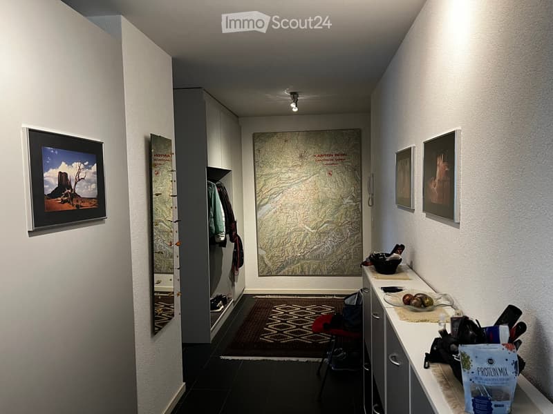 A modern hallway with a large mirror, a framed picture, a small table with items, a chair, and a rug on the floor.