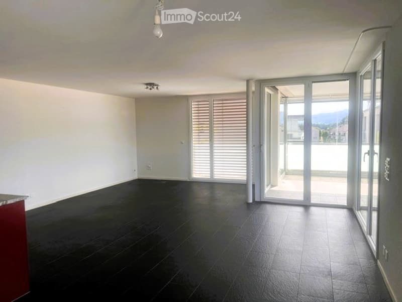 Empty room with dark wooden flooring, white walls, large sliding glass doors leading to a balcony, and a visible light fixture on the ceiling.