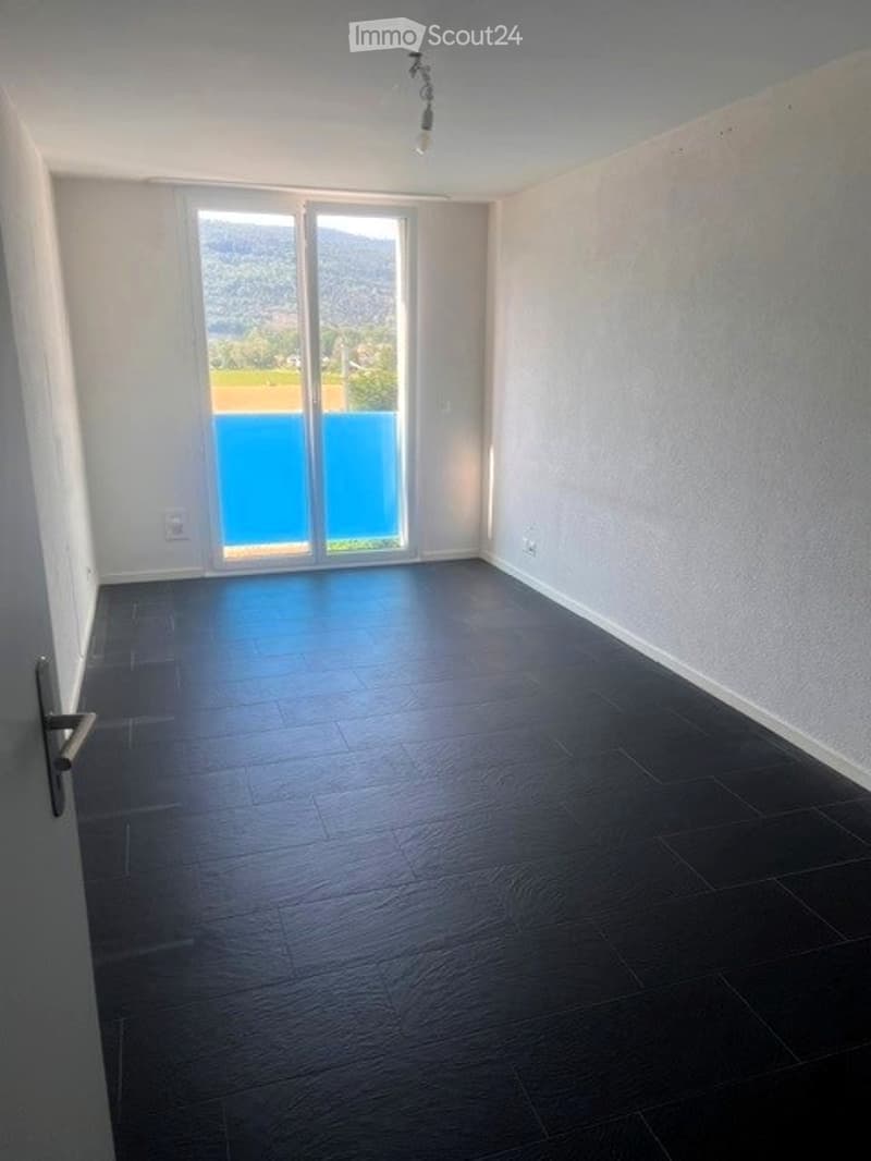 Empty room with dark wooden flooring, large glass sliding doors leading to a balcony with a view of a blue pool and mountains.