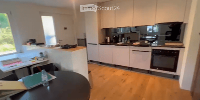 Modern kitchen with white cabinets, stainless steel appliances, wooden flooring, and a small dining area with a table and chairs.