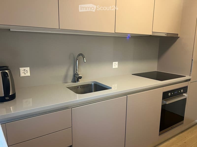 Modern kitchen with light-colored cabinets, a stainless steel sink, a built-in oven, and an electric kettle on the counter.