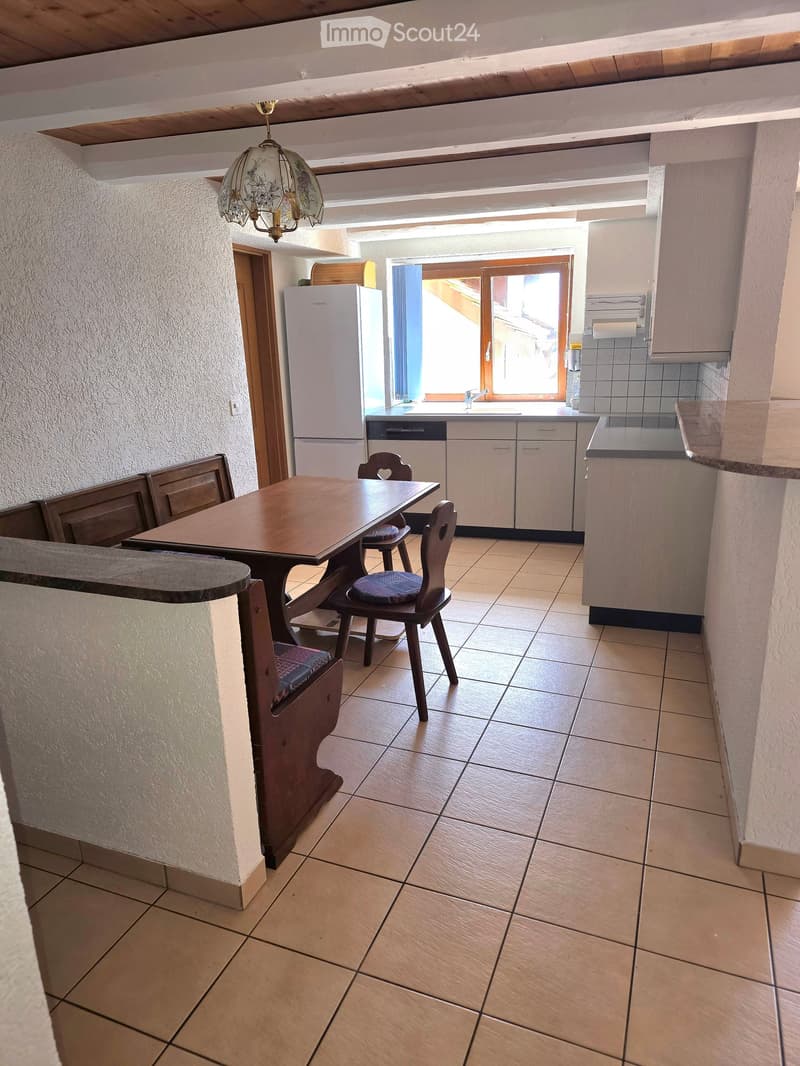 Dining area with wooden table and chairs, white refrigerator, wooden ceiling beams, tiled floor, kitchen with white cabinets, sink, and dishwasher