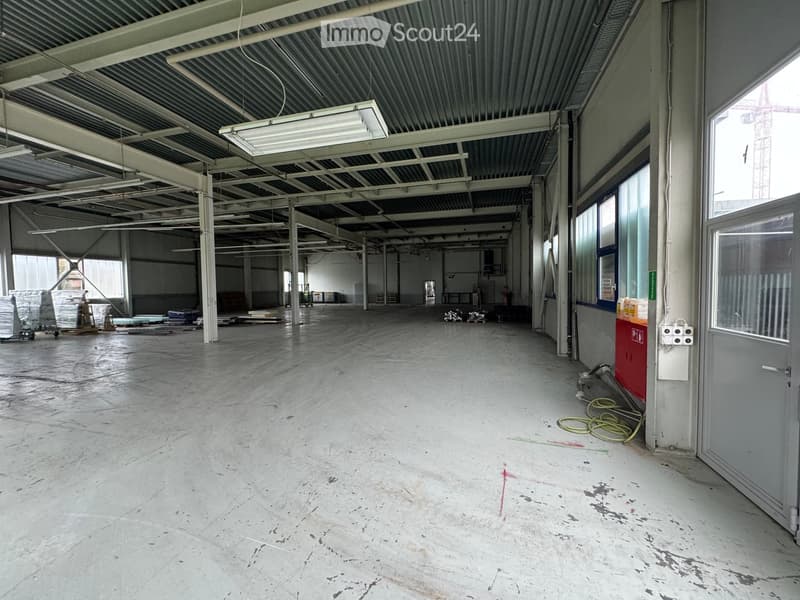 large open space, metal ceiling, fluorescent lighting, wide aisles, windows on the far wall, red pillar at the corner, door at the end