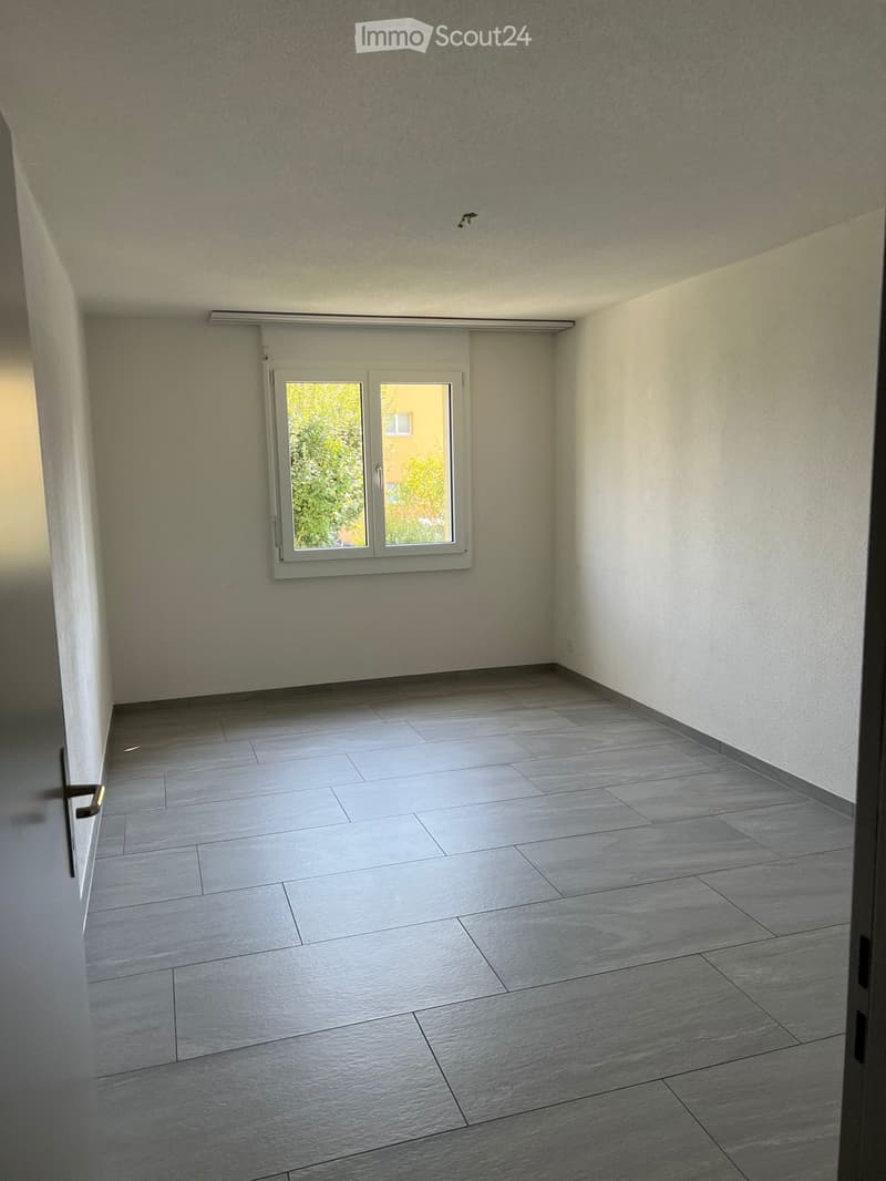 Empty room with grey tiled floor, white walls, and a window with white frame and blinds.
