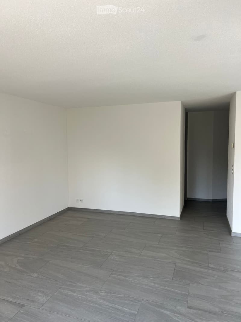 Empty room with grey tiled floor and white walls, featuring a doorway leading to another space.