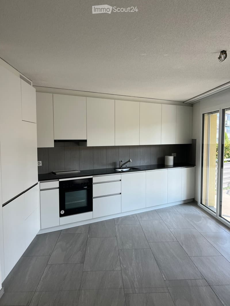 Modern kitchen with white cabinets, grey tiled backsplash, and grey tiled floor. Features an oven, sink, and faucet.