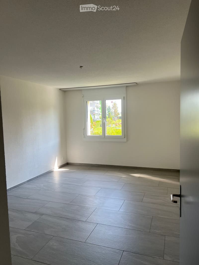 Empty room with grey tiled floor, white walls, and a large window with blinds. No furniture or equipment present.
