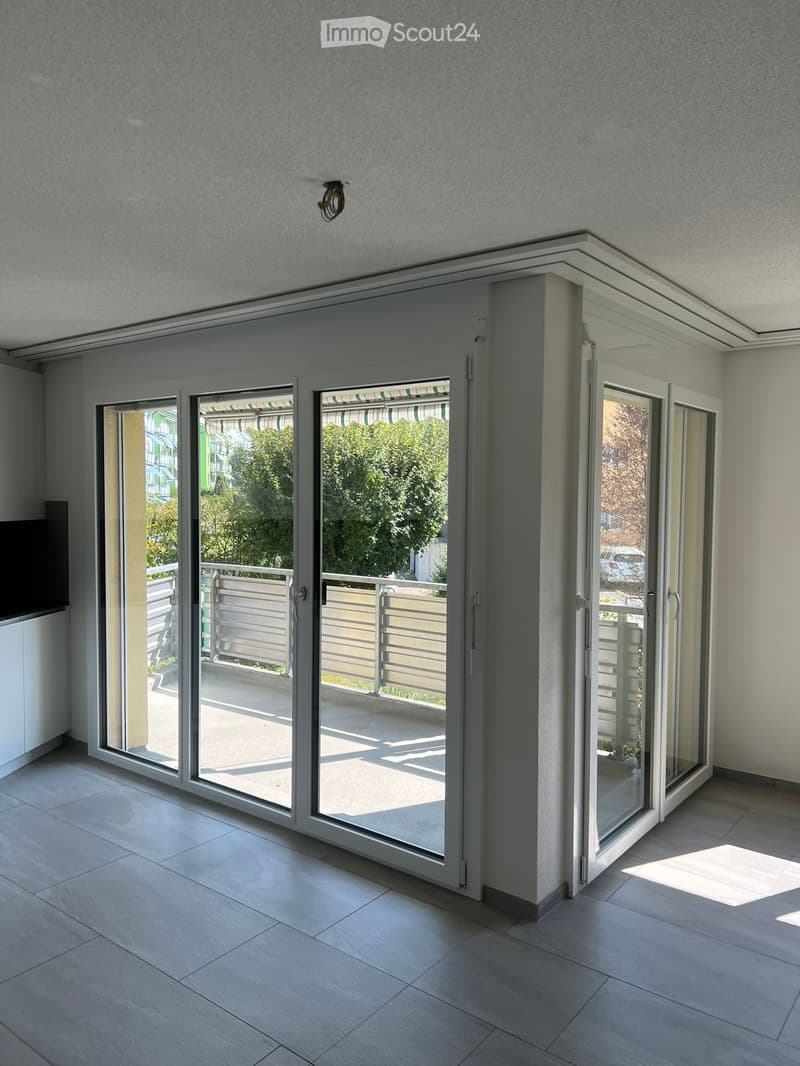 Modern interior space with large sliding glass doors leading to a balcony, tiled floor, and visible outdoor area with greenery.