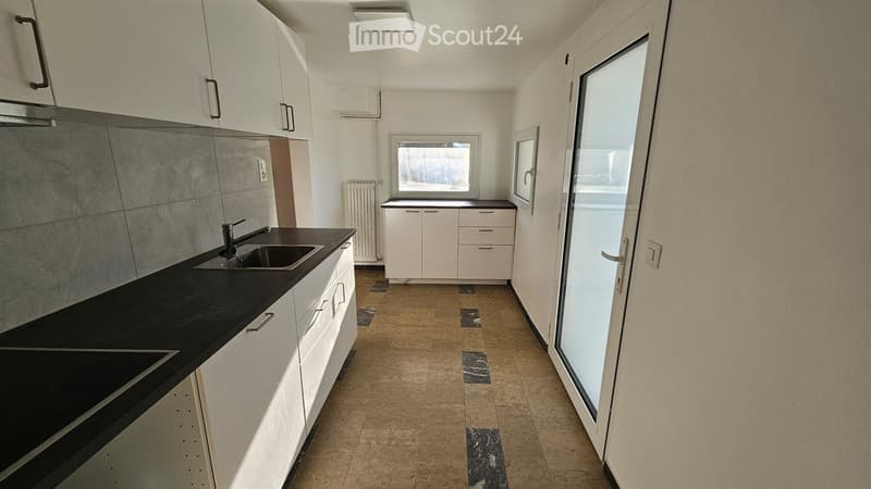 Empty kitchen with white cabinets, black countertops, and a sink. The space includes a window and a sliding glass door leading outside.