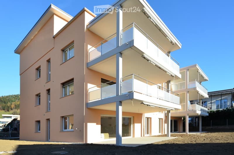 Modern two-story building with light pink facade, large windows, and multiple balconies with glass railings.