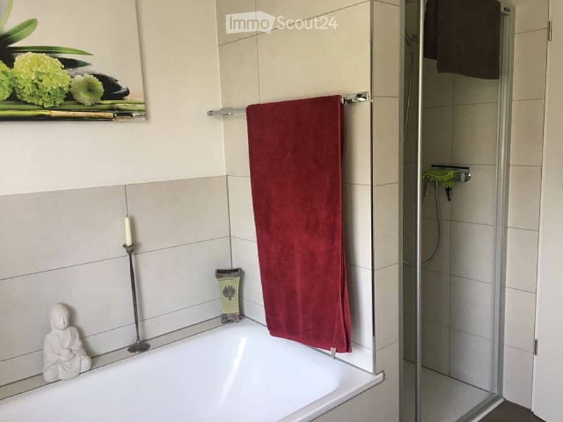 Modern bathroom with a white bathtub, red towel hanging on a rod, a small decorative statue, a candle, and a glass-enclosed shower area.