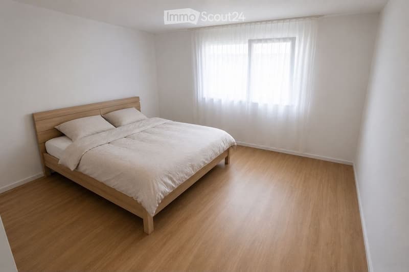A modern bedroom with a wooden bed, light-colored bedding, and a large window with sheer curtains. The room features light wooden flooring and white walls.