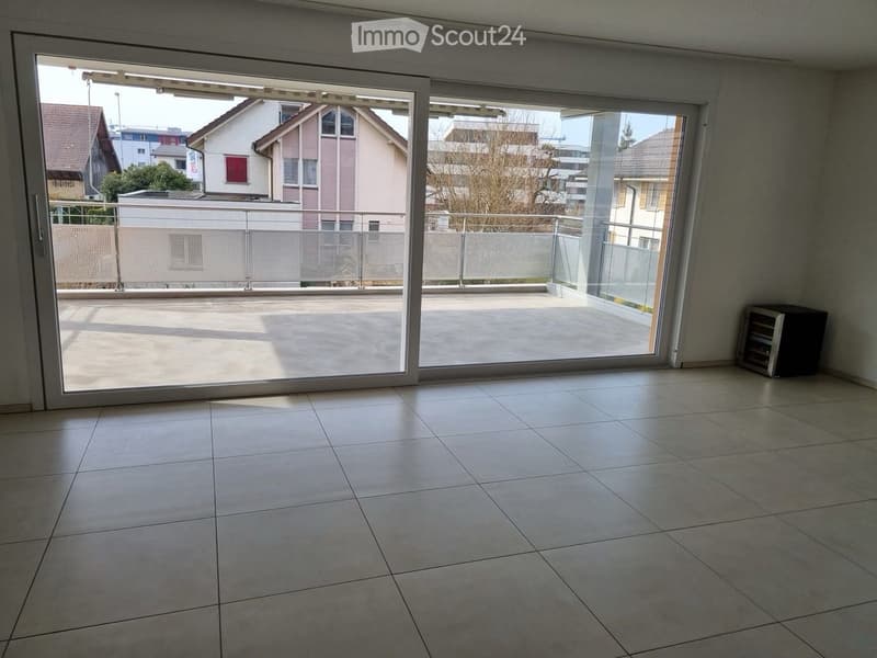 Empty room with tiled floor, large sliding glass doors leading to a balcony or terrace area, and a small black cabinet in the corner.