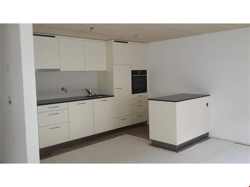 Modern kitchen with white cabinets, black countertops, and stainless steel appliances. Features a sink with a faucet, an oven, and a central island counter.