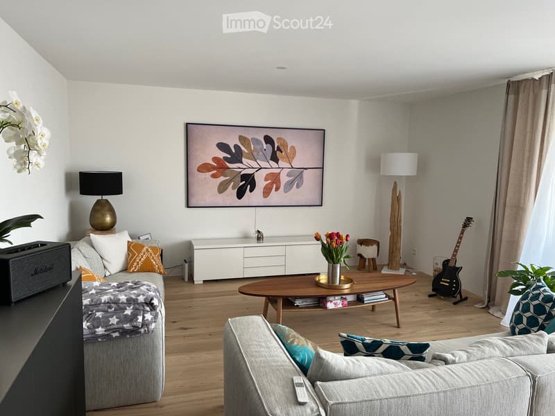 Living room with sofa, coffee table, TV, center table, speaker, white walls, flooring, plants, lamp, cabinet, artwork, remote control