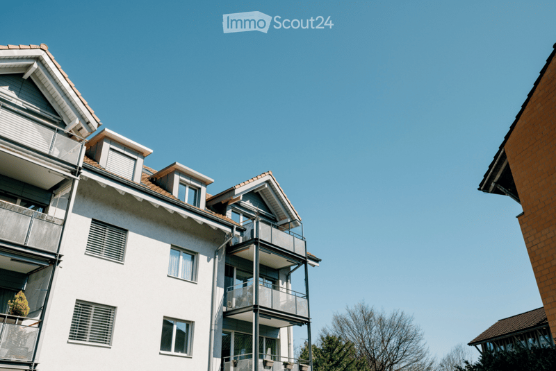 Multi-story residential building with balconies, white facade, and brown roof.