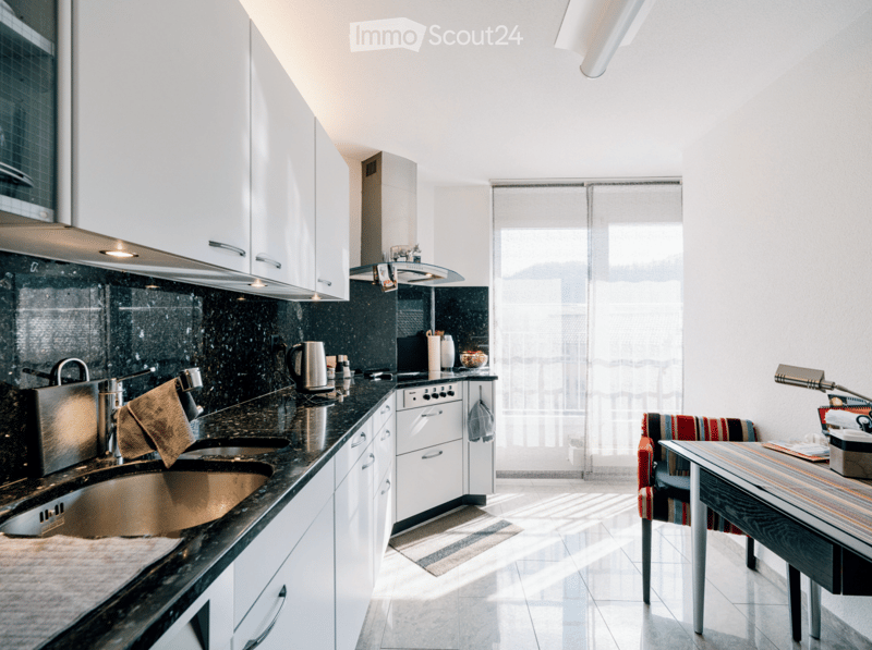 Modern kitchen with white cabinets, black granite countertops, stainless steel appliances, and a small dining area with a colorful chair and table.