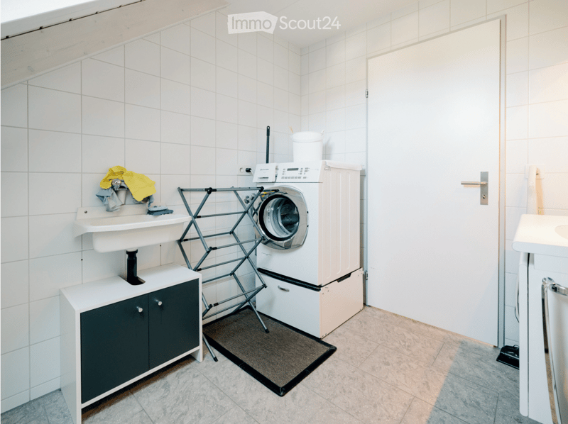 Bathroom with a washing machine, sink, cabinet, and laundry rack. The walls are tiled, and the floor is tiled as well.