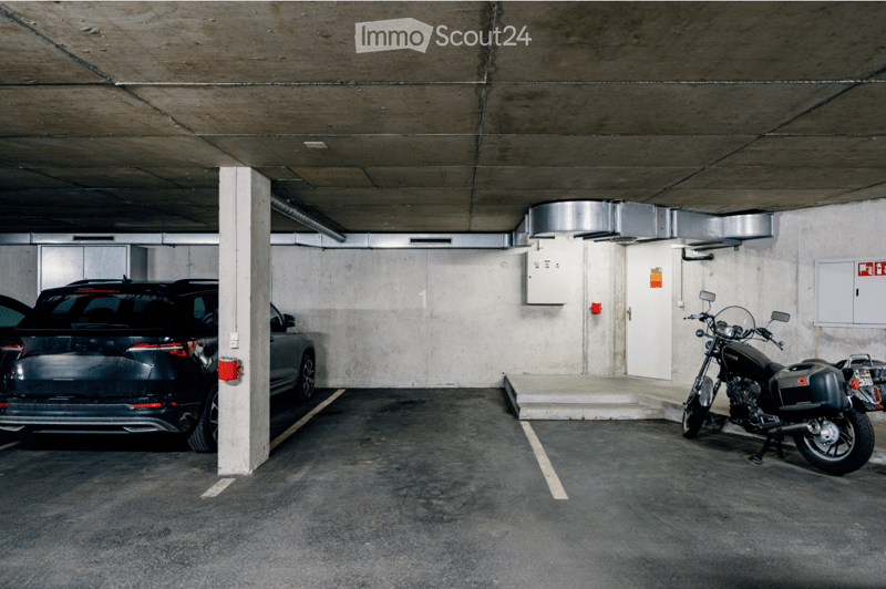 Underground parking area with concrete walls and ceiling, featuring a parked SUV and a motorcycle, along with a white pillar and electrical panel.