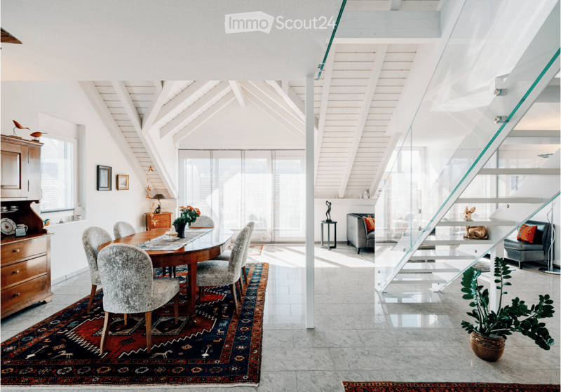 Bright, open-plan living and dining area with wooden dining table, chairs, sofa, and decorative items.