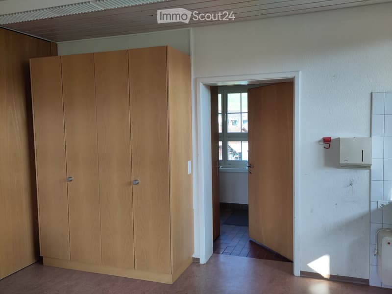 Empty room with wooden cabinet, open doorway leading to another room, tiled walls, and a visible light switch.